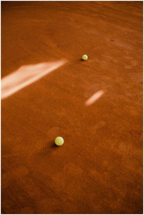Tennis balls scattered on a clay court with dramat