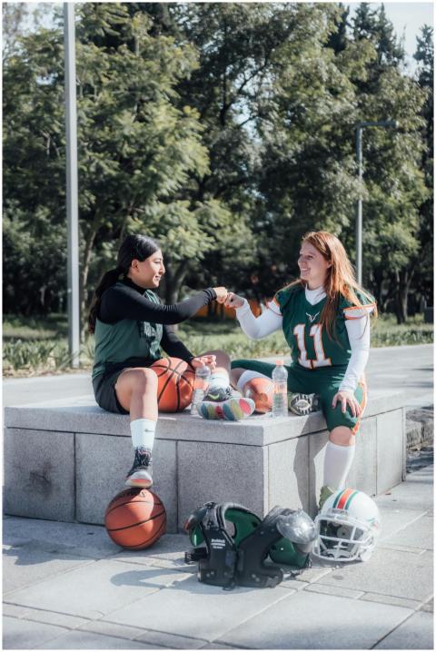 Two women in sportswear fist bump while sitting ou