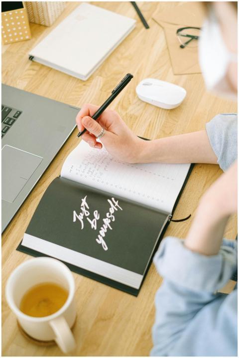 A woman writes notes in an open notebook with 'Jus