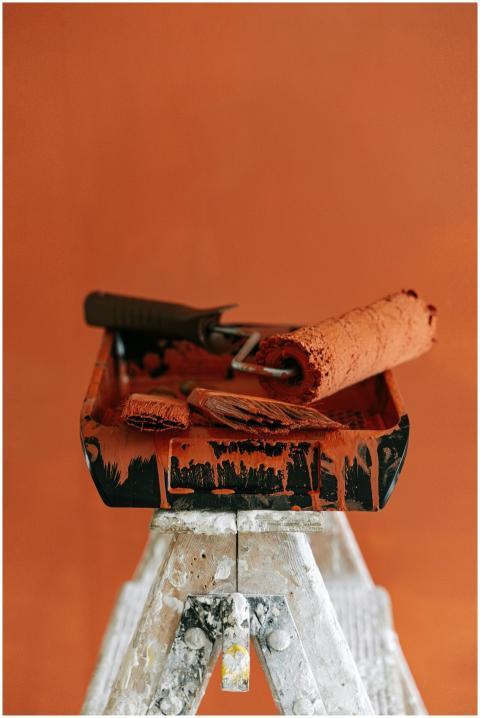 A stepladder holds paint tools for a vibrant orang