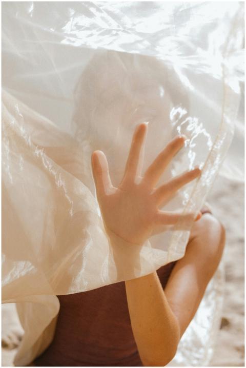 A woman obscured by sheer fabric reaches her hand