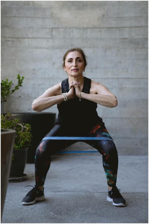 Elderly woman performing squat exercise indoors, p