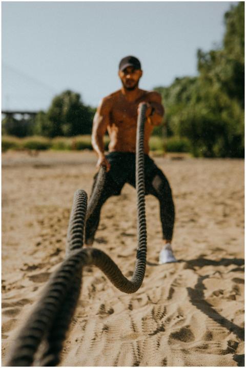 Fit man training with battle ropes on a sandy outd