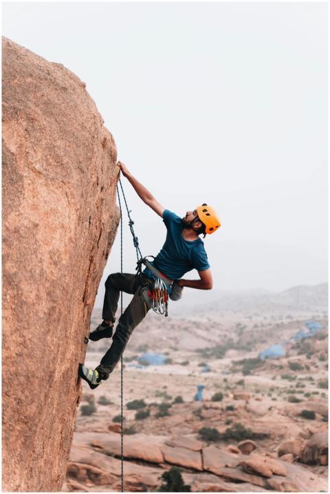 A man in a helmet rock climbing a steep cliff outd