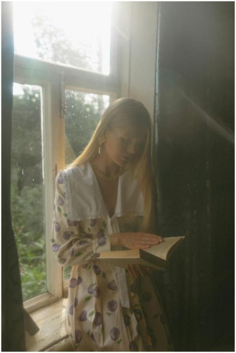 A young woman in stylish attire reads a book by a