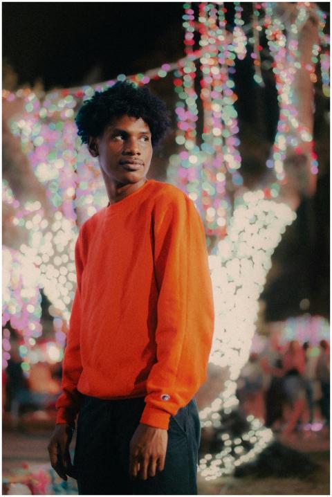A young man in an orange sweater stands amidst vib
