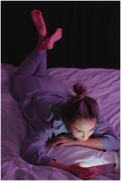 A woman lying on a bed using her smartphone at nig