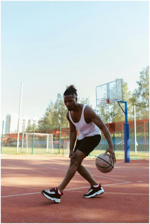 Young man dribbling basketball on outdoor court du