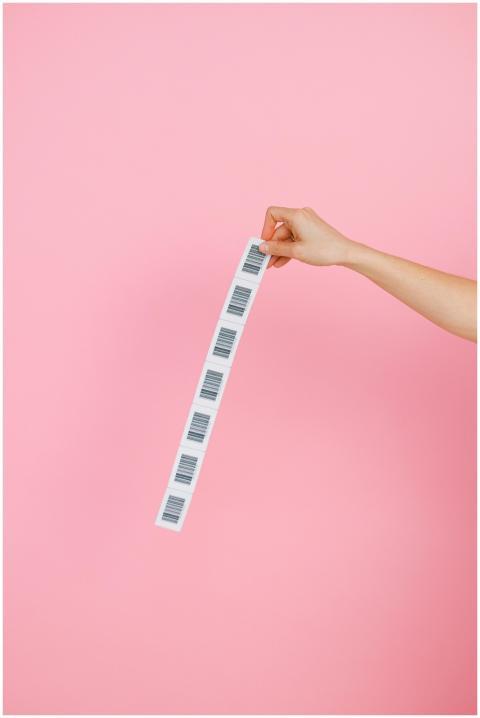 A hand holds a strip of barcodes against a pink ba