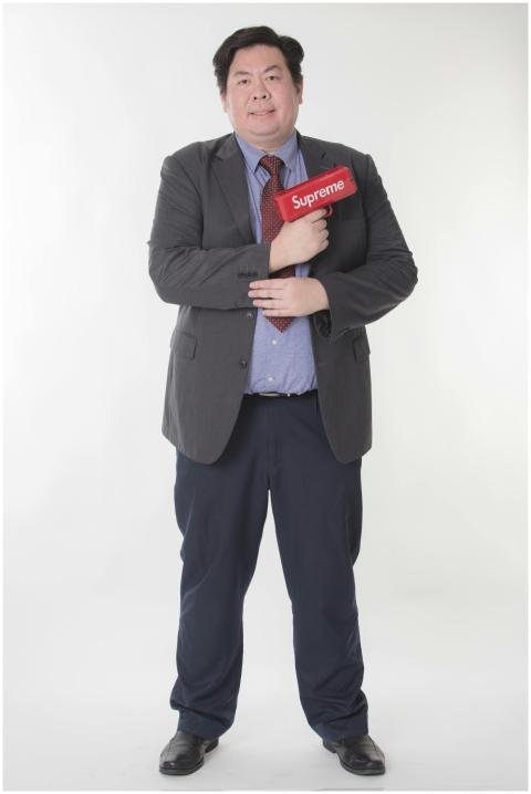 Asian man in a suit holds a red toy gun against a