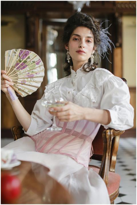 Woman in vintage attire holding a fan and a wine g