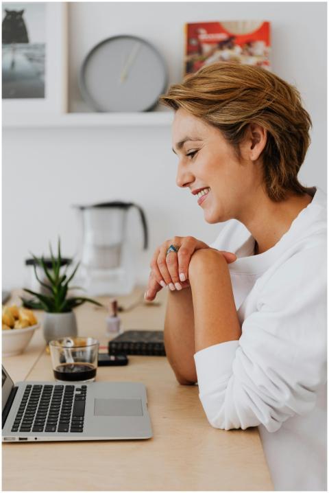 Woman in white top smiling while using a laptop at