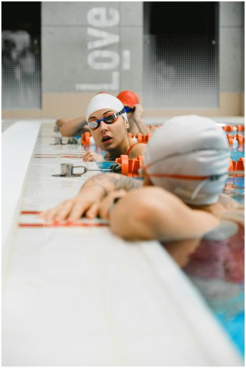 Swimmers in goggles and caps converse at an indoor
