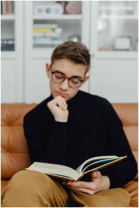 Teenager wearing glasses reading a book on a couch