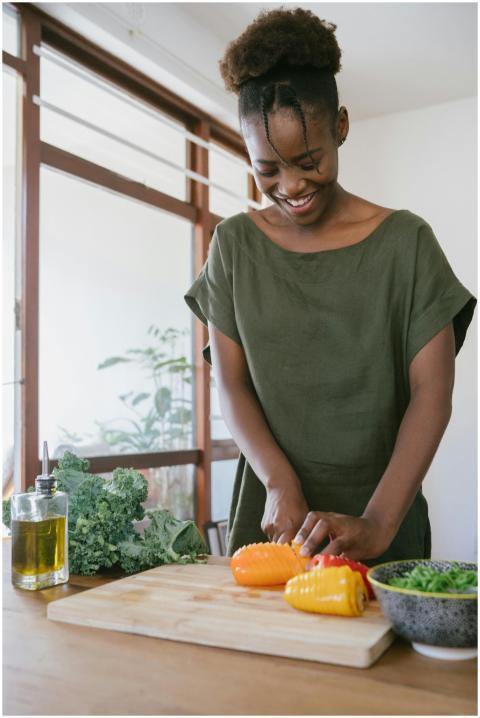 Smiling woman in kitchen slicing bell peppers, pro