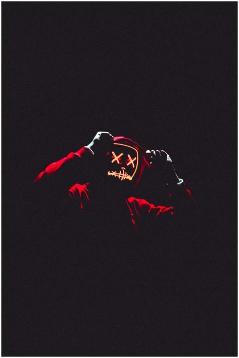 A person in a glowing neon mask and hoodie in a da