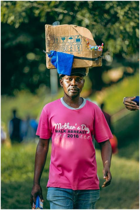 A man carries goods on his head, wearing a pink sh