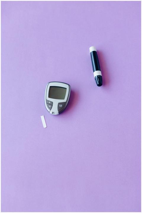 Flat lay of glucose monitor and lancet on a purple