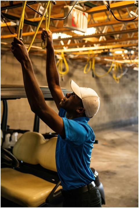 A man wearing a cap works on wiring above a golf c