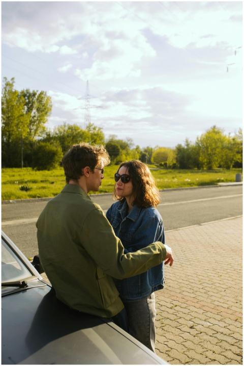 Young couple outdoors, leaning on a car, embracing