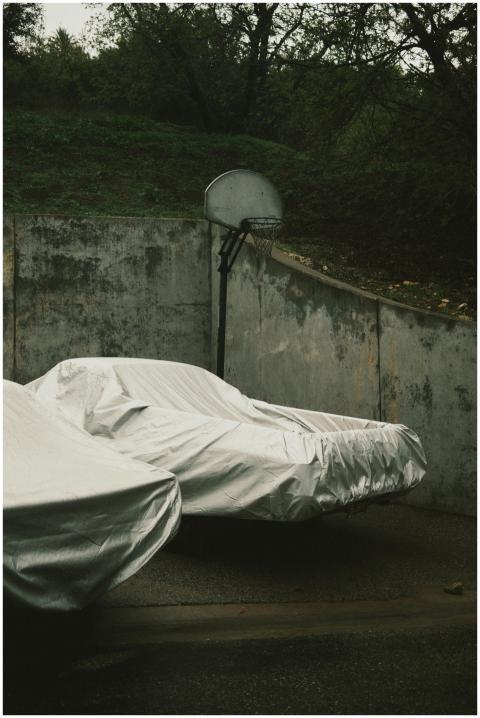 Covered cars beneath a basketball hoop in a moody,
