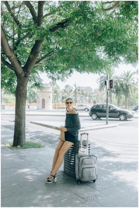 Fashionable woman sitting with luggage on sunny ci