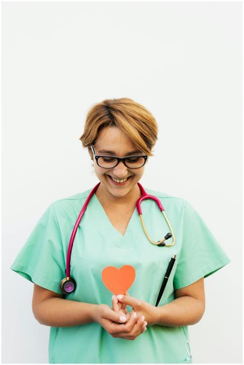 Smiling nurse in scrubs holding a paper heart symb