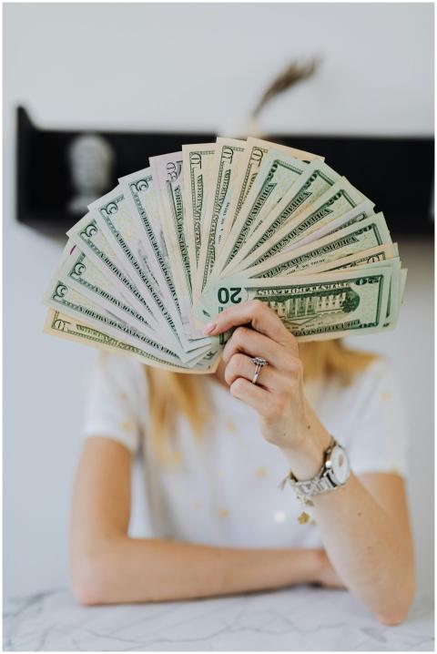 A person holding a fan of US dollar bills, symboli