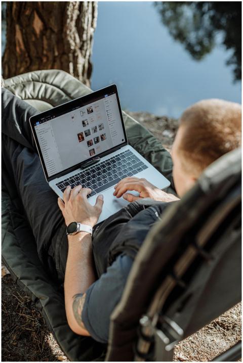 Young man working on a laptop outdoors by a lake,