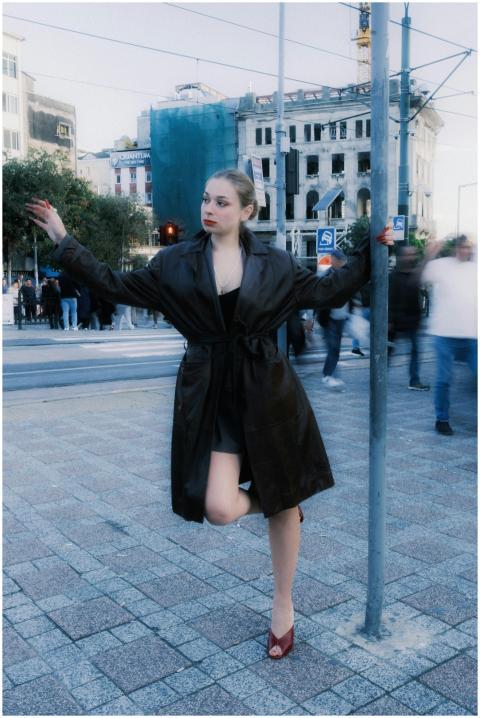 Stylish woman in dark coat leaning on pole with bl