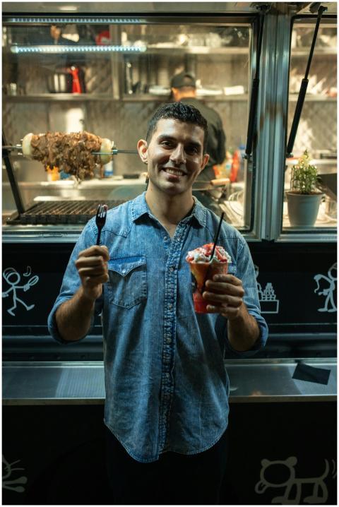 A man smiling while holding street food and a fork