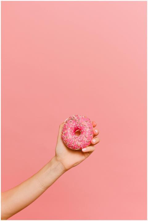 A hand holding a pink sprinkled donut against a ma