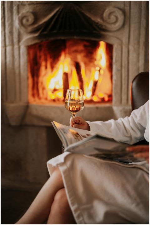Woman relaxing by the fireplace with a book and wi