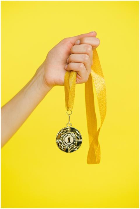 Close-up of a hand holding a gold medal symbolizin