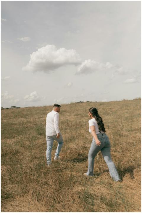 A couple in casual attire walks through a grassy f