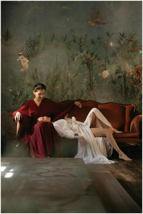 Two women in elegant attire pose artfully on a vin