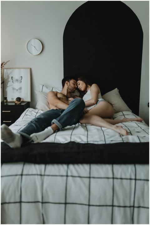 A young couple embraces intimately on a bed in a w