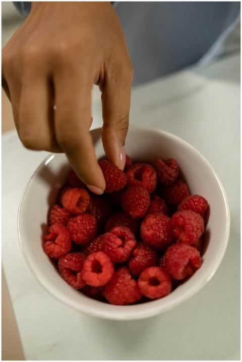 A hand with manicured nails grabbing fresh raspber