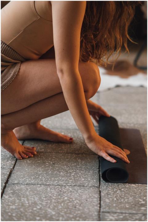 A woman crouching to roll out a yoga mat on a tile