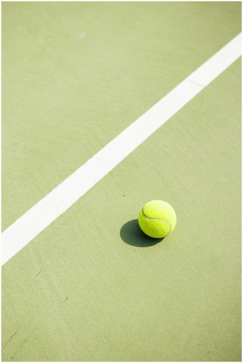 Tennis ball casting shadow on a sunlit green court