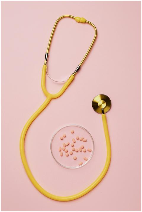 Flat lay of yellow stethoscope with pink pills on