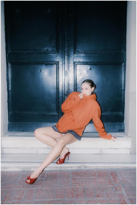 Chic woman in an orange hoodie poses at night, cap
