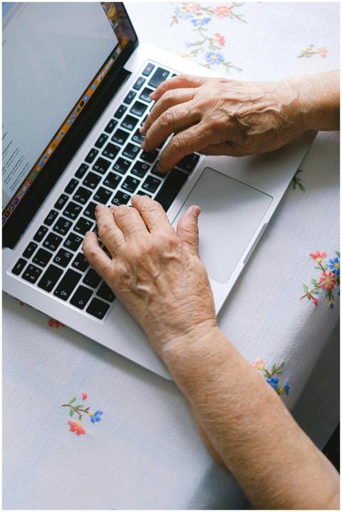 Elderly hands typing on a laptop keyboard at home,