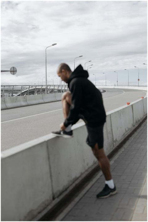 Man in hoodie tying shoelace on concrete barrier i