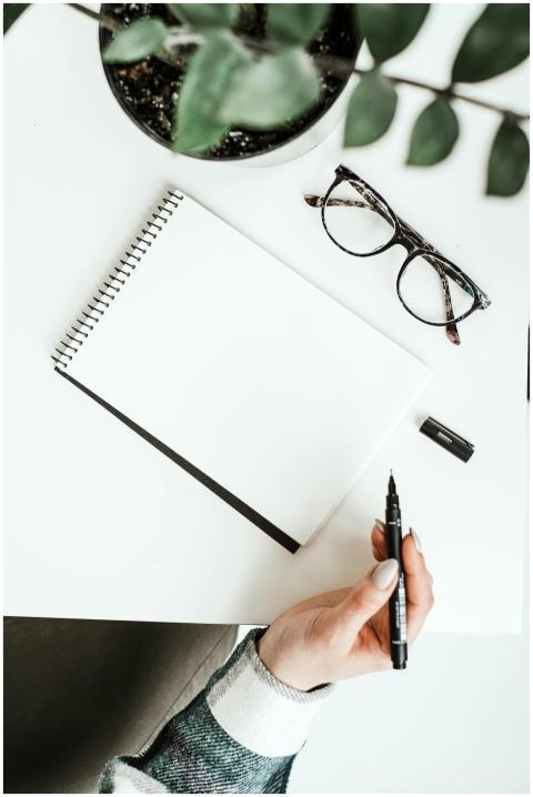 Flat lay of a blank notebook with pen, eyeglasses,