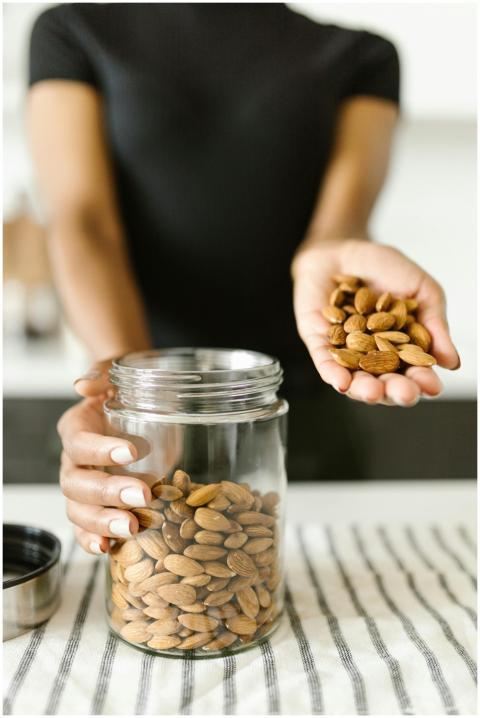 A person pours almonds from hand into a glass jar,