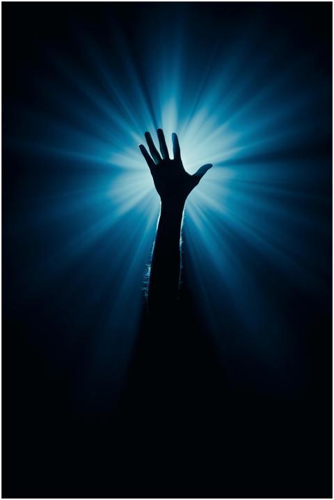 Silhouette of a raised hand against a dramatic blu