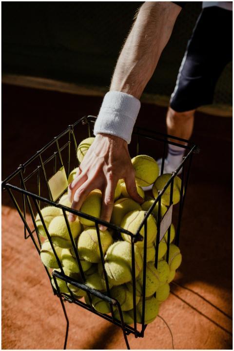 A tennis player collecting balls from a basket on