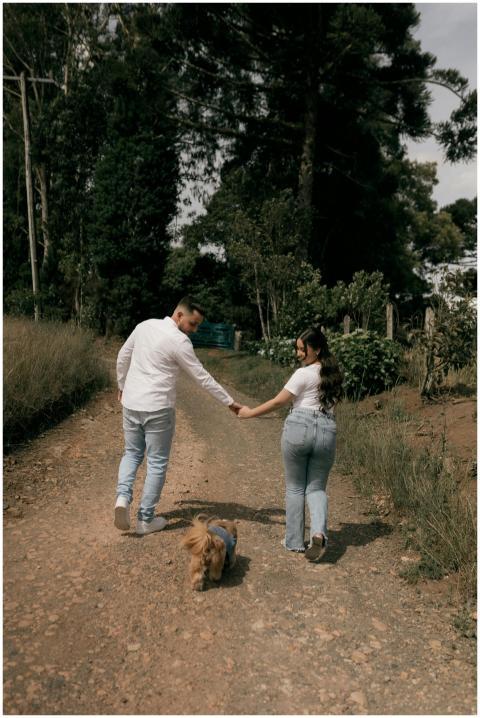 A couple walking hand in hand with a dog on a rust