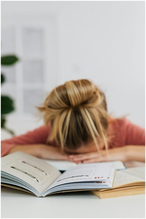A tired student resting their head on a table surr
